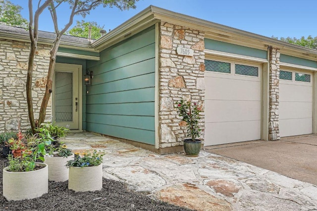 property entrance with a garage, stone siding, and driveway