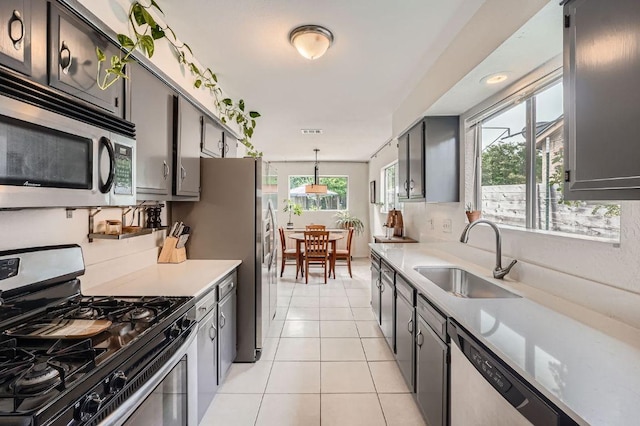 kitchen with appliances with stainless steel finishes, a sink, light countertops, light tile patterned floors, and hanging light fixtures