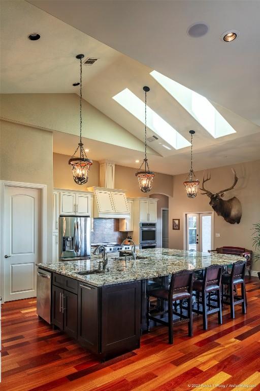 kitchen featuring stainless steel appliances, a sink, a skylight, dark wood finished floors, and high vaulted ceiling