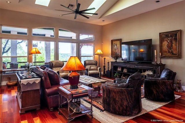 living area with a skylight, a ceiling fan, wood finished floors, high vaulted ceiling, and recessed lighting