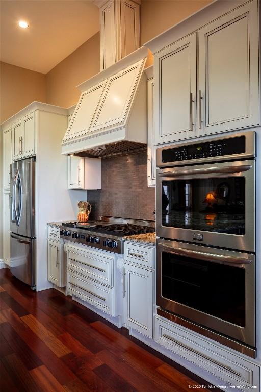 kitchen with appliances with stainless steel finishes, custom range hood, tasteful backsplash, dark wood-style flooring, and dark stone counters