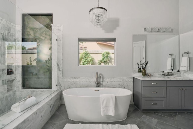 full bathroom featuring a chandelier, tile walls, a soaking tub, vanity, and wainscoting