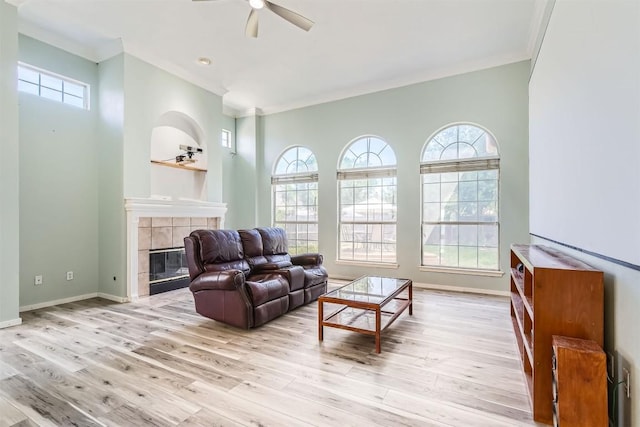 living room featuring ceiling fan, ornamental molding, a tiled fireplace, wood finished floors, and baseboards