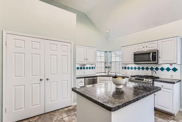 kitchen featuring stainless steel appliances, white cabinetry, dark countertops, backsplash, and high vaulted ceiling