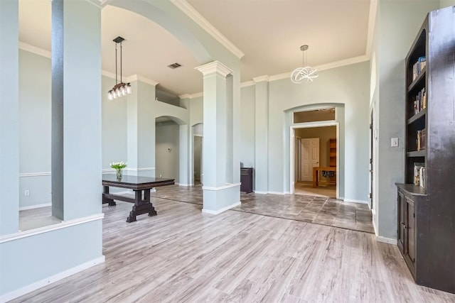foyer featuring arched walkways, crown molding, light wood-style flooring, baseboards, and ornate columns