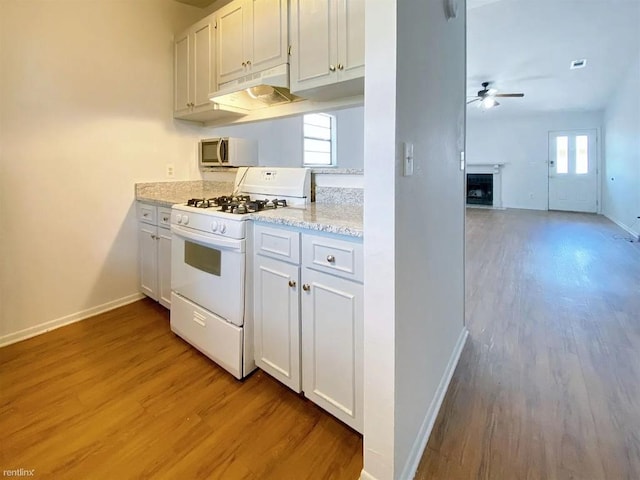 1604 Mill St Unit B, San Marcos, TX 78666 - kitchen with white range with gas cooktop, under cabinet range hood, light wood-type flooring, ceiling fan, and a fireplace