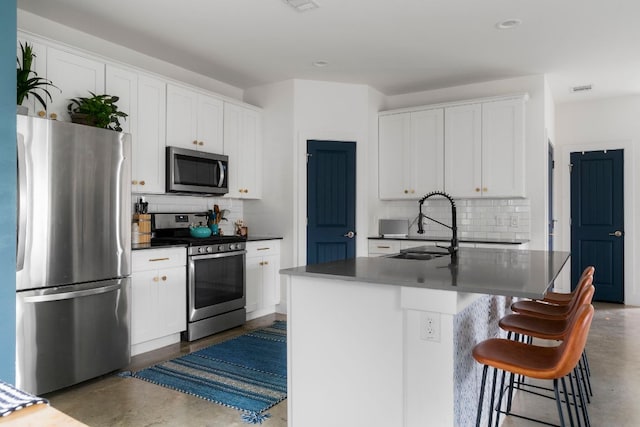 kitchen with appliances with stainless steel finishes, concrete floors, a sink, decorative backsplash, and dark countertops