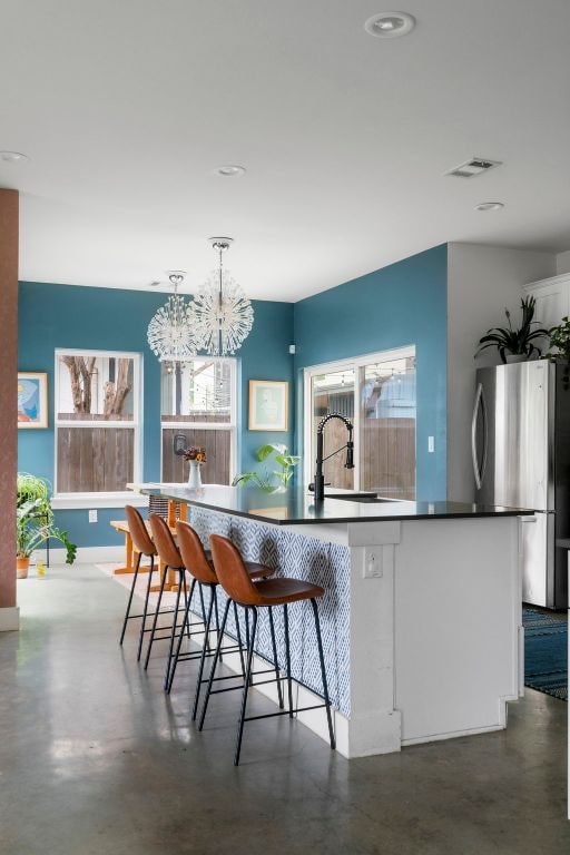 kitchen with a sink, freestanding refrigerator, finished concrete flooring, a chandelier, and hanging light fixtures