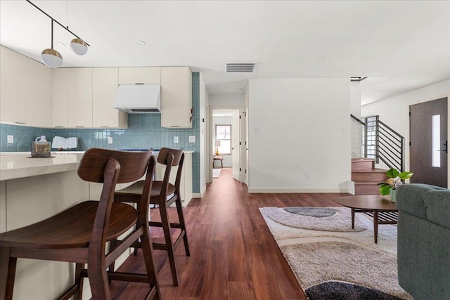 kitchen with custom exhaust hood, dark wood-style floors, tasteful backsplash, and decorative light fixtures