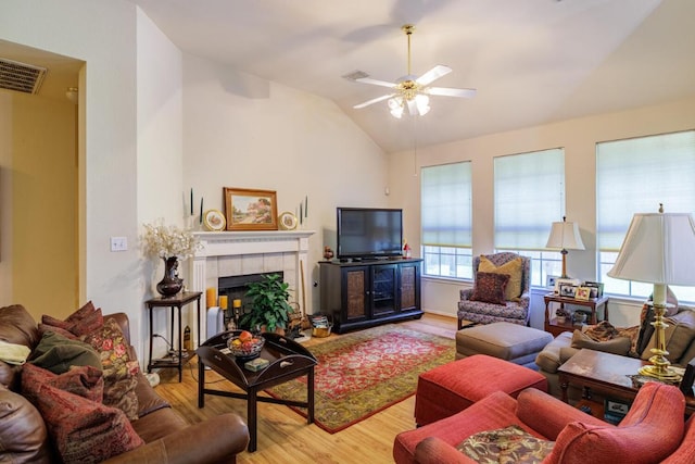 living area with lofted ceiling, wood finished floors, ceiling fan, and a tiled fireplace