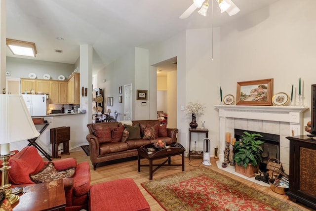 living room with a ceiling fan, light wood-style flooring, and a tiled fireplace