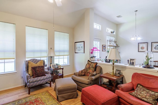living area with light wood-style flooring, a ceiling fan, a chandelier, and baseboards