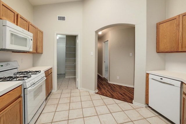 kitchen with white appliances, arched walkways, a towering ceiling, light countertops, and light tile patterned floors