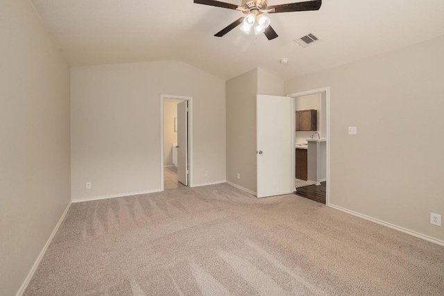 unfurnished bedroom featuring light carpet, lofted ceiling, baseboards, connected bathroom, and a ceiling fan