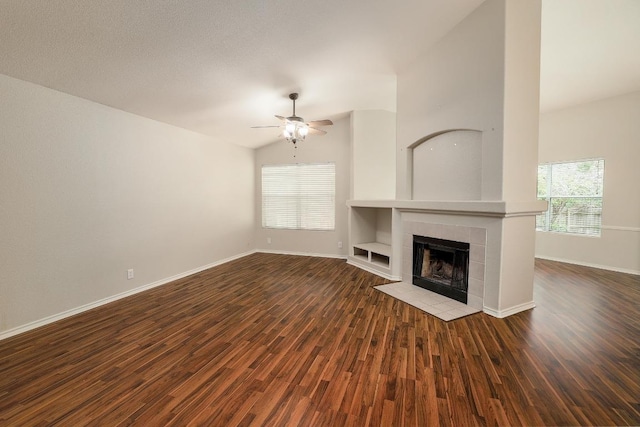 unfurnished living room with ceiling fan, baseboards, dark wood finished floors, vaulted ceiling, and a tiled fireplace