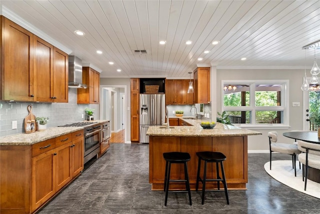 2601 W 49th St, Austin, TX 78731 - kitchen with wall chimney range hood, stainless steel appliances, a peninsula, recessed lighting, and brown cabinets