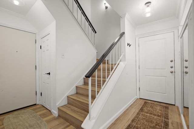 entryway with wood finished floors, stairs, and crown molding