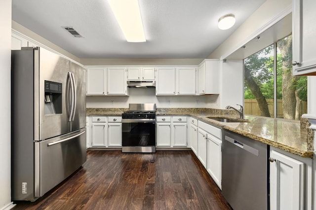 kitchen with appliances with stainless steel finishes, a sink, stone countertops, under cabinet range hood, and white cabinetry