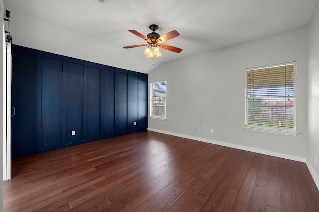 unfurnished room with wood finished floors, a ceiling fan, baseboards, vaulted ceiling, and a barn door