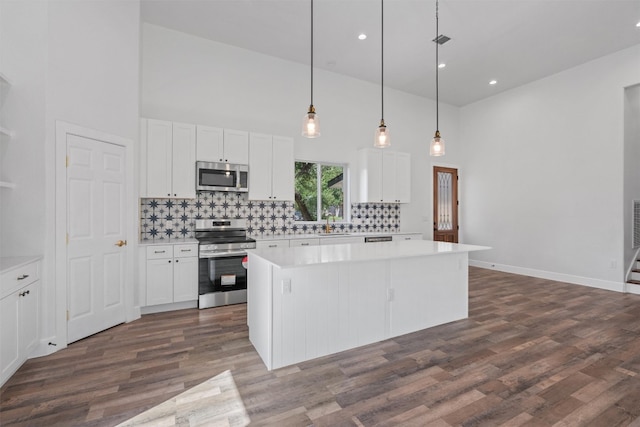 kitchen featuring appliances with stainless steel finishes, a towering ceiling, dark wood-style flooring, a kitchen island, and white cabinetry