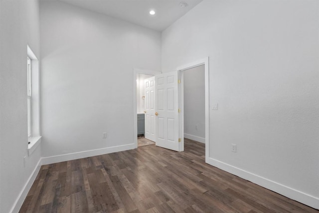 unfurnished bedroom with wood finished floors, a towering ceiling, baseboards, ensuite bathroom, and recessed lighting