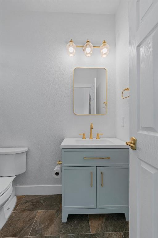 half bathroom with baseboards, vanity, and toilet