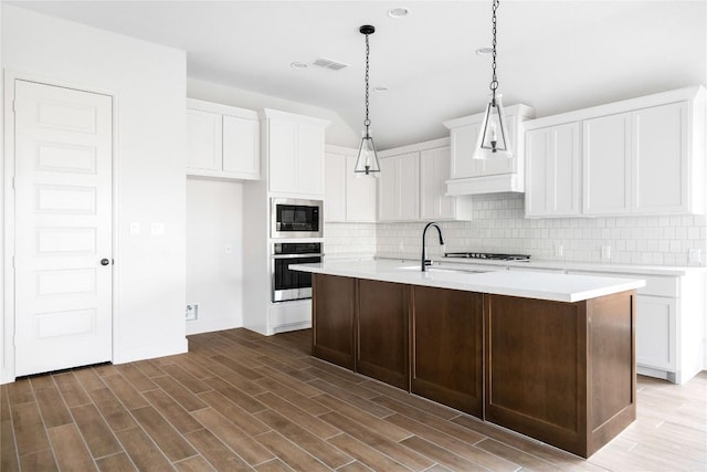 639 Bay Breeze Dr, Kyle, TX 78640 - kitchen with stainless steel appliances, decorative backsplash, white cabinetry, light countertops, and an island with sink