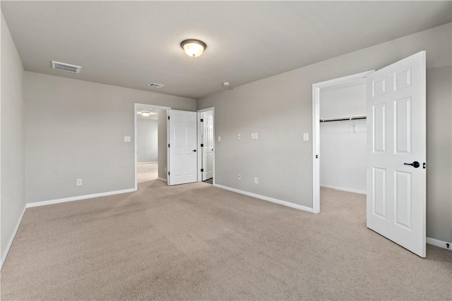 unfurnished bedroom with baseboards, light colored carpet, a walk in closet, and a closet