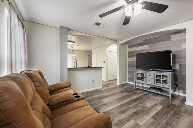 living area featuring an accent wall, baseboards, wooden walls, a ceiling fan, and dark wood-type flooring