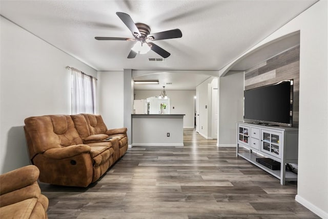 living area featuring a ceiling fan, baseboards, and dark wood-type flooring