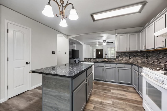 kitchen featuring gray cabinetry, white gas range oven, arched walkways, a sink, and wood finished floors