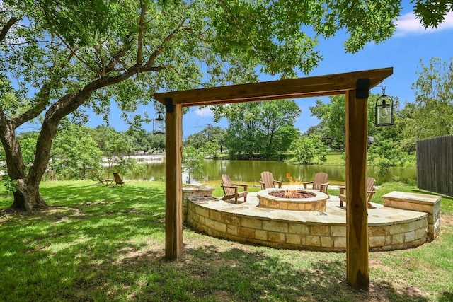view of grassy yard featuring an outdoor fire pit, a water view, and view of wooded area