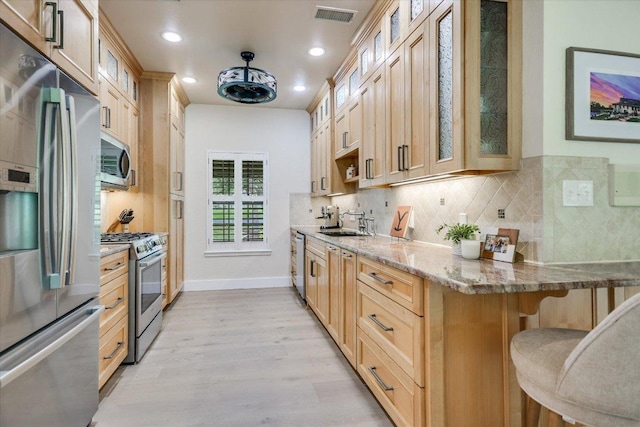 3301 Arrowhead Cir, Round Rock, TX 78681 - kitchen with stainless steel appliances, a kitchen bar, light stone countertops, light wood-style flooring, and decorative backsplash