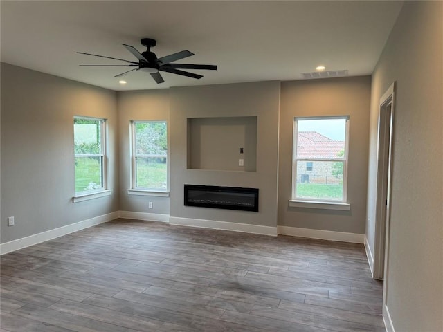 3318 Bay W Blvd, Horseshoe Bay, TX 78657 - unfurnished living room featuring healthy amount of natural light, a glass covered fireplace, wood finished floors, recessed lighting, and a ceiling fan