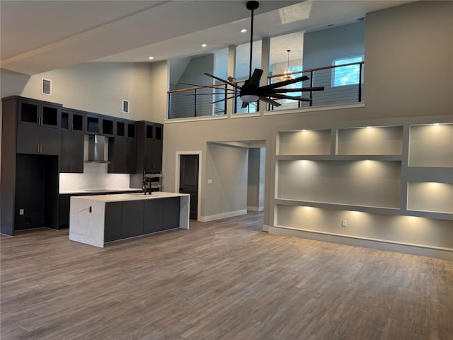 3318 Bay W Blvd, Horseshoe Bay, TX 78657 - kitchen with wall chimney exhaust hood, dark cabinets, modern cabinets, a center island with sink, and light countertops