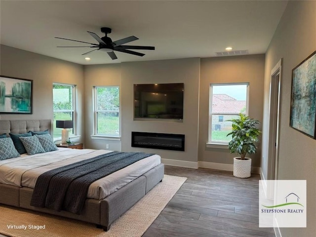 3318 Bay W Blvd, Horseshoe Bay, TX 78657 - bedroom with multiple windows, wood finished floors, a glass covered fireplace, recessed lighting, and ceiling fan