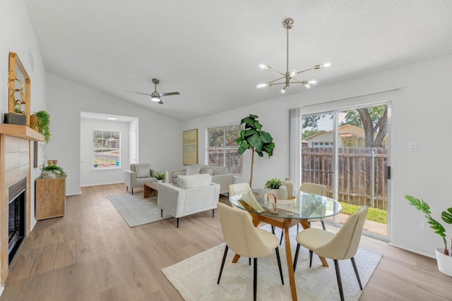 dining space featuring light wood-style flooring, vaulted ceiling, a tile fireplace, a chandelier, and ceiling fan