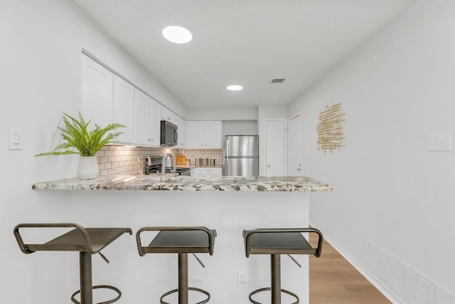 kitchen with appliances with stainless steel finishes, a peninsula, backsplash, white cabinets, and a kitchen breakfast bar