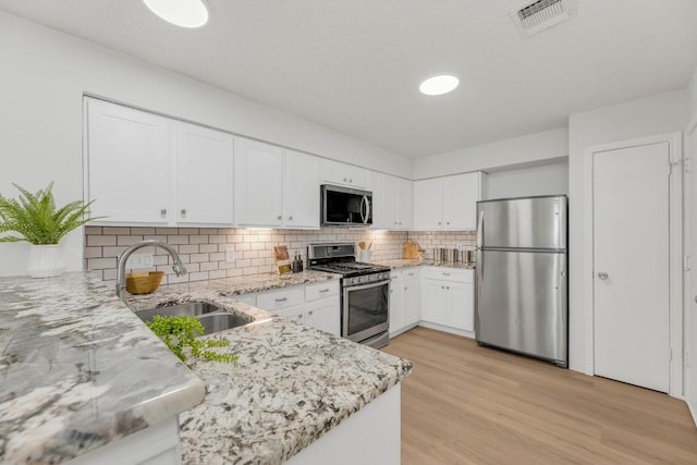 kitchen with stainless steel appliances, a sink, light stone counters, light wood-type flooring, and tasteful backsplash
