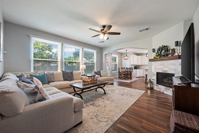 living room with arched walkways, a ceiling fan, dark wood-type flooring, and a tile fireplace