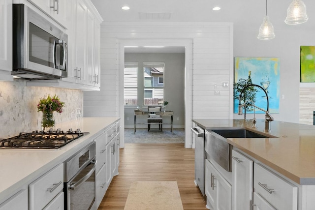 716 Dayridge Dr, Dripping Springs, TX 78620 - kitchen featuring appliances with stainless steel finishes, a sink, light wood-style floors, tasteful backsplash, and white cabinetry