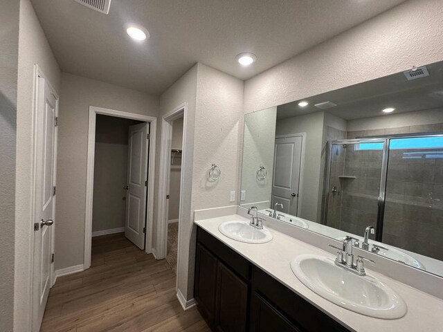 152 Mason Hill Ln, Georgetown, TX 78628 - full bathroom featuring a stall shower, wood finished floors, a textured wall, double vanity, and a walk in closet