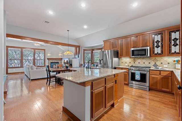 11036 Cherisse Dr, Austin, TX 78739 - kitchen featuring appliances with stainless steel finishes, a stone fireplace, vaulted ceiling, brown cabinetry, and light stone countertops