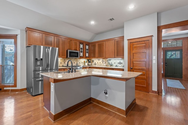 11036 Cherisse Dr, Austin, TX 78739 - kitchen featuring stainless steel appliances, backsplash, an island with sink, light stone countertops, and light wood-type flooring