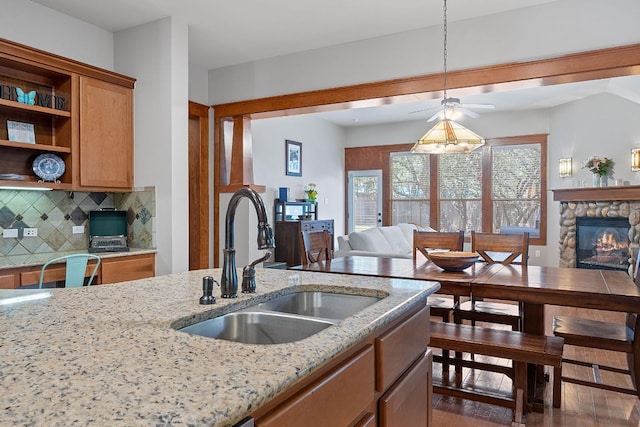 11036 Cherisse Dr, Austin, TX 78739 - kitchen featuring light stone counters, backsplash, ceiling fan, open floor plan, and a stone fireplace