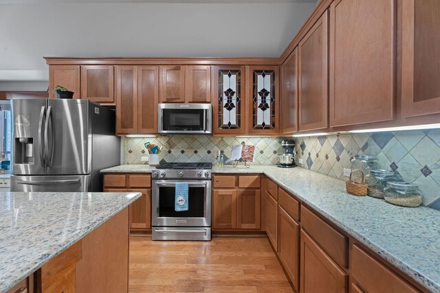 11036 Cherisse Dr, Austin, TX 78739 - kitchen featuring appliances with stainless steel finishes, glass insert cabinets, light stone counters, light wood finished floors, and tasteful backsplash