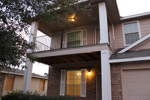 view of exterior entry featuring a balcony, brick siding, and a garage