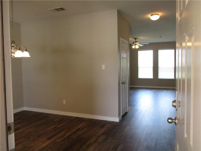 empty room featuring a ceiling fan, baseboards, dark wood-style floors, and a chandelier