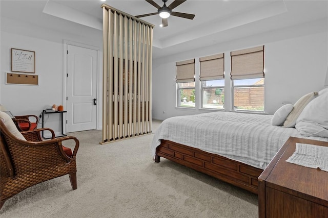 bedroom with a tray ceiling, light colored carpet, and a ceiling fan