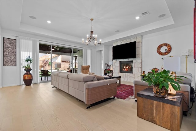 living area with a raised ceiling, light wood-style flooring, a chandelier, a fireplace, and recessed lighting